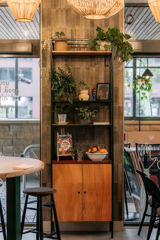 Statement tiled wall with large windows either side. Black metal and wood cabinet holds plants, framed artwork and a cookbook